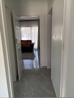 Un pasillo que conduce a una habitación con cama y ventana con cortinas.