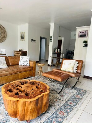 A living room with a brown leather sofa, a wooden coffee table, and a patterned rug. - Exquisite Art Deco 2 bed Apartment - 2395 (Harare)