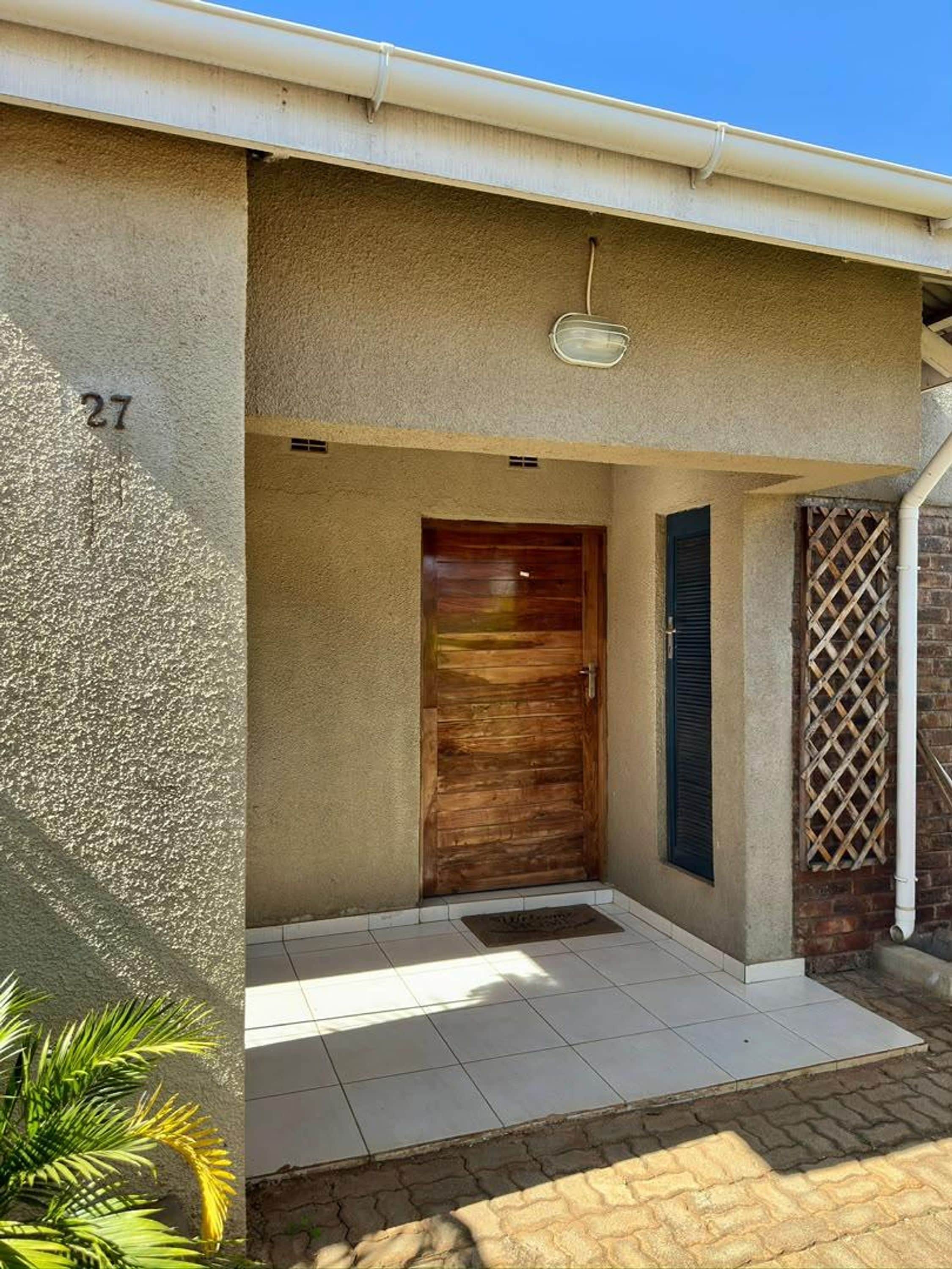 A residential entrance with a number '27' on the wall, a wooden door, and a small porch area.