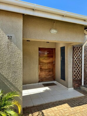 A residential entrance with a number '27' on the wall, a wooden door, and a small porch area. - Exquisite Art Deco 2 bed Apartment - 2395 (Harare)