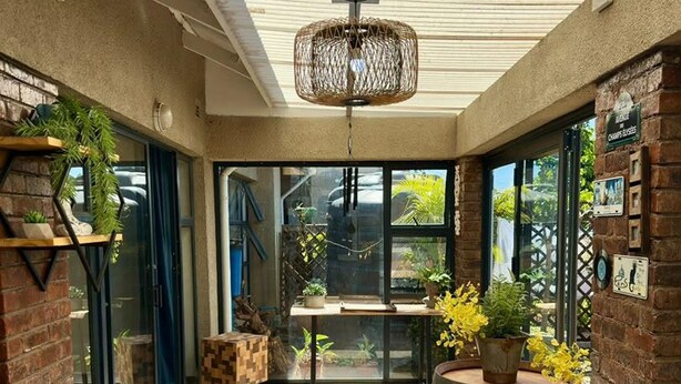 Uma área de varanda coberta com mesa, cadeiras e plantas em vasos.