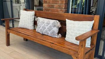A wooden bench with patterned cushions in front of a brick wall and glass doors.