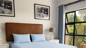 Quarto com cama, mesas de cabeceira, janela com vista e duas imagens emolduradas na parede.