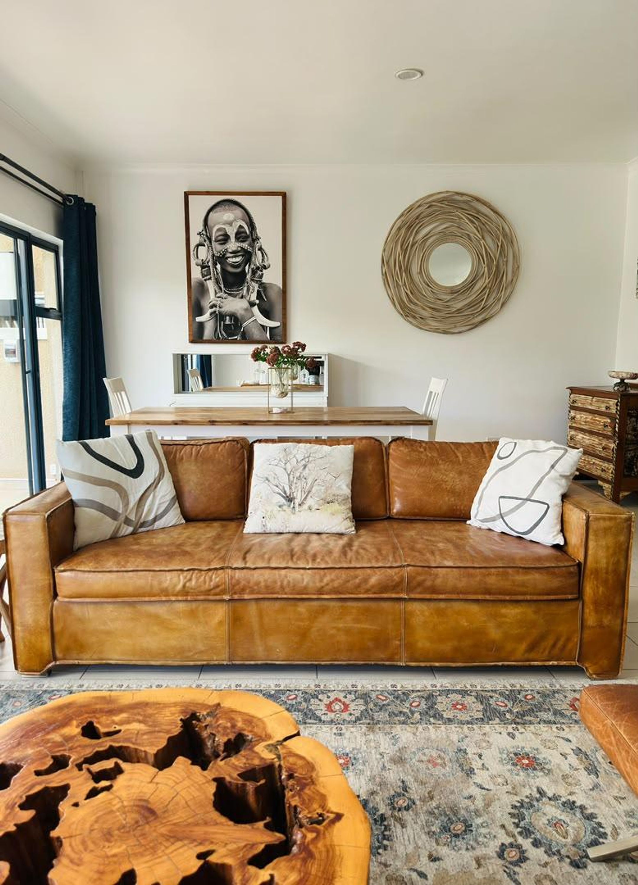 A living room with a brown leather sofa, a wooden coffee table, a patterned rug, a framed picture on the wall, and a mirror above a shelf.