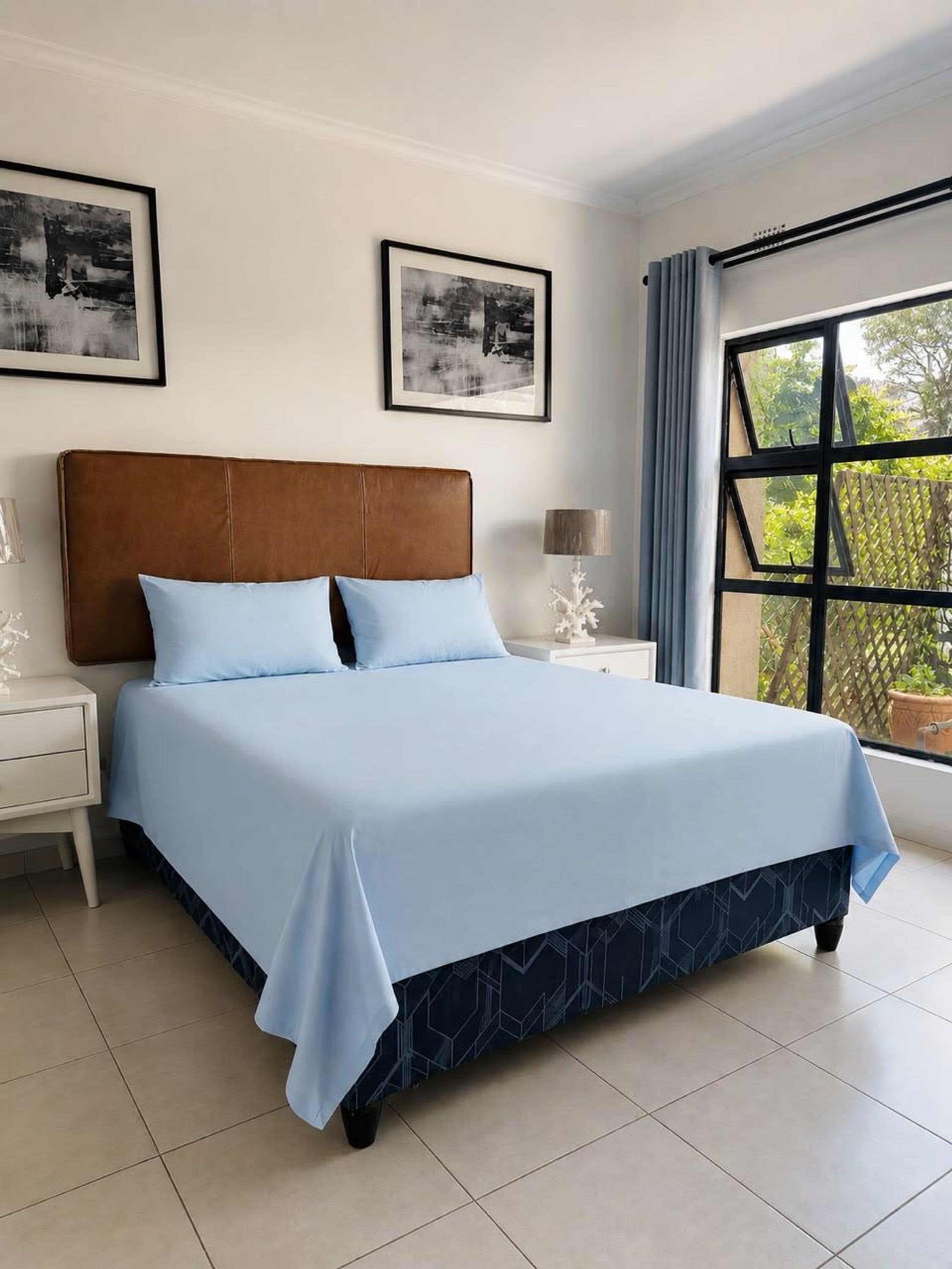 A bedroom with a bed, nightstands, a window with a view, and two framed pictures on the wall.