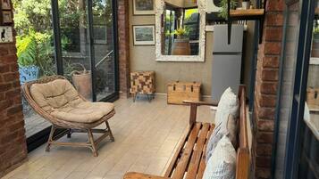 A sunlit room with a wooden bench, wicker chair, and a large mirror.