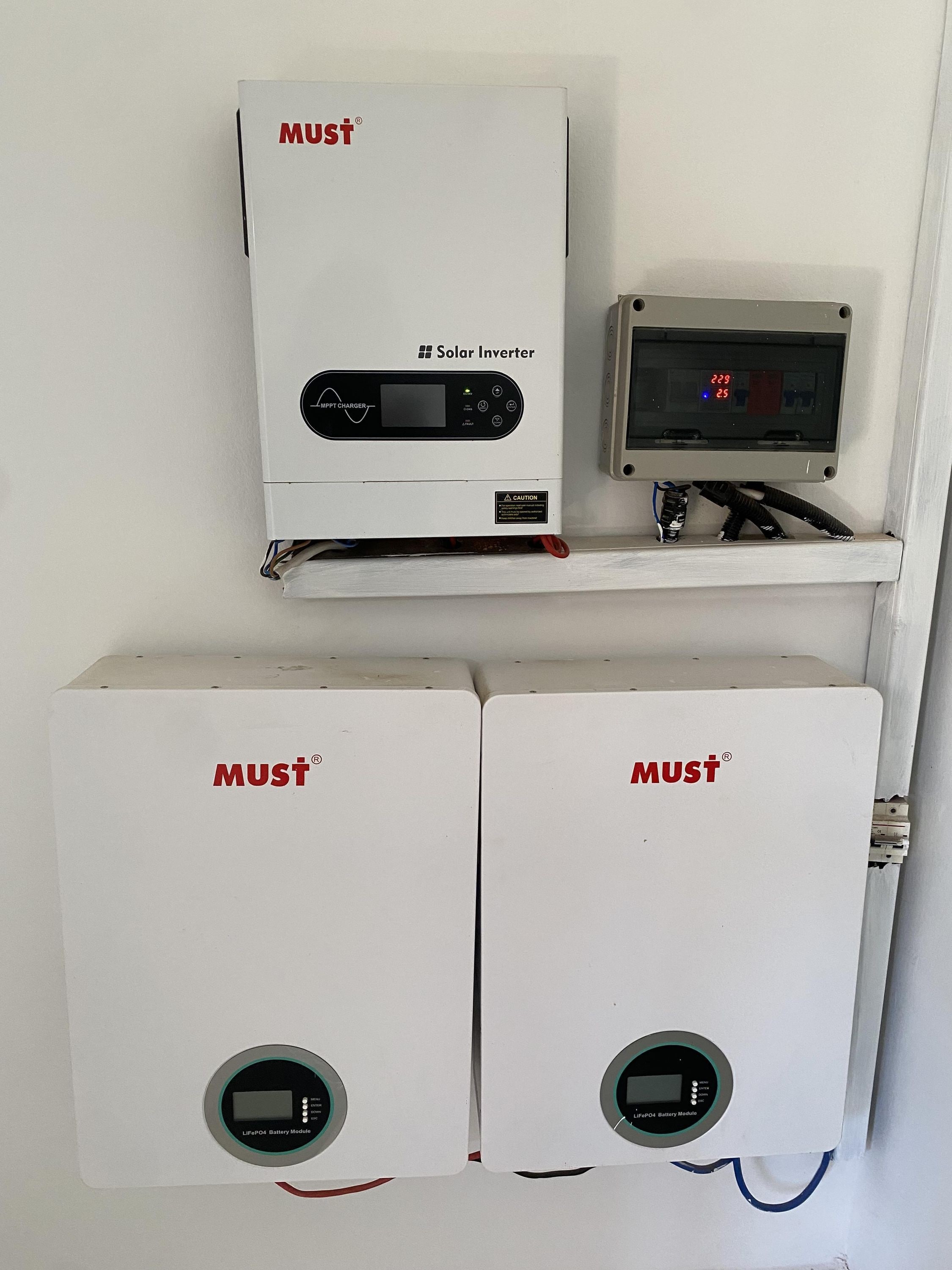 A solar inverter and two battery modules labeled 'MUST' on a wall.
