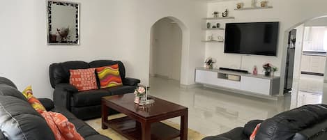 A modern living room with a black leather sofa set, a wooden coffee table, and a flat-screen TV mounted on the wall.