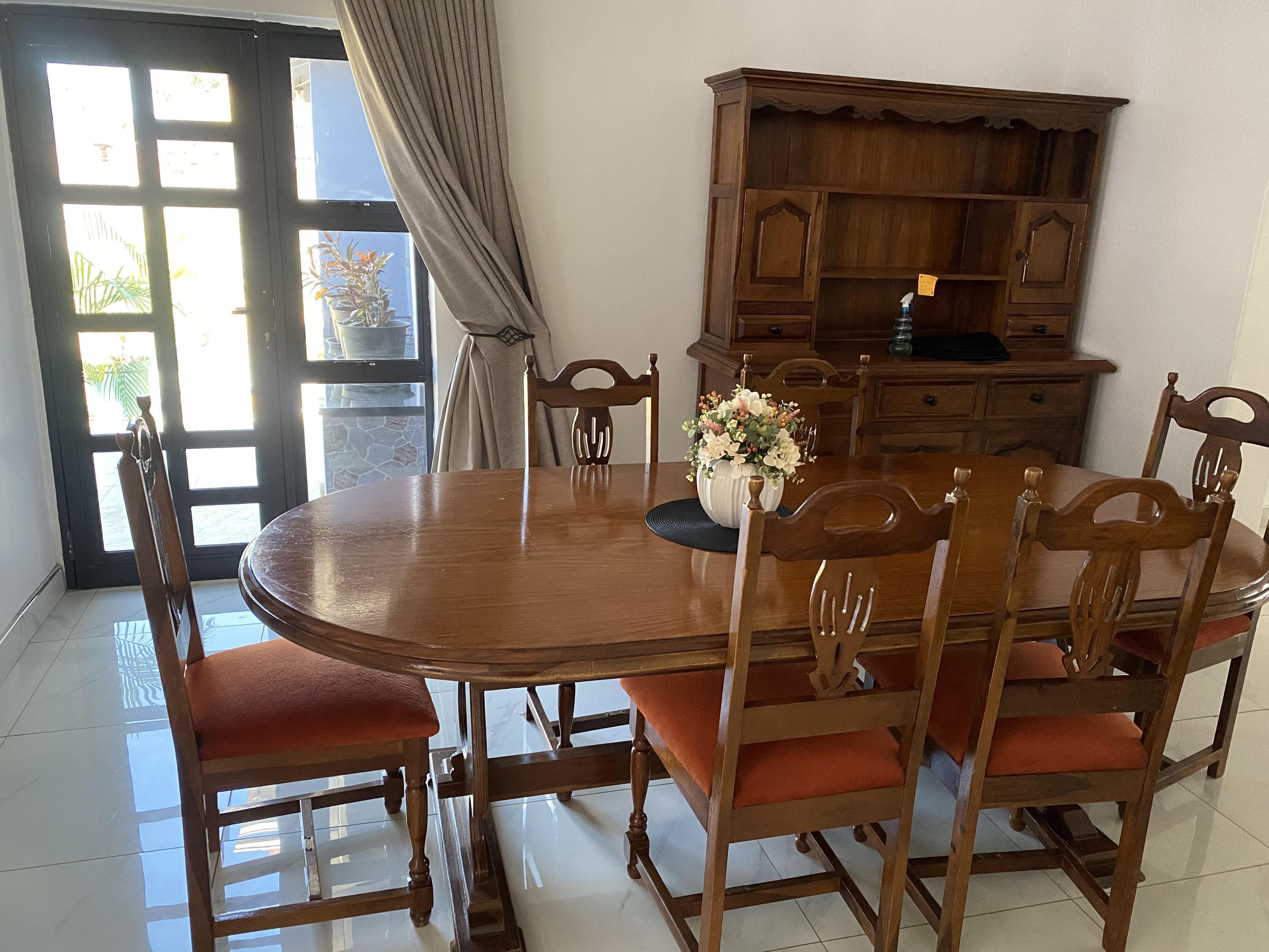 Un comedor con una mesa de madera, sillas, un jarrón con flores y un armario de madera.