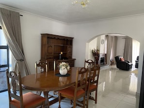 A dining area with a wooden table and chairs, a vase with flowers, and a wooden cabinet. - Newly Renovated 4 Bedroom Guesthouse - 2389 (Harare)