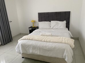 A bed with a headboard, a bedside table with a lamp, and a curtain. - Newly Renovated 4 Bedroom Guesthouse - 2389 (Harare)