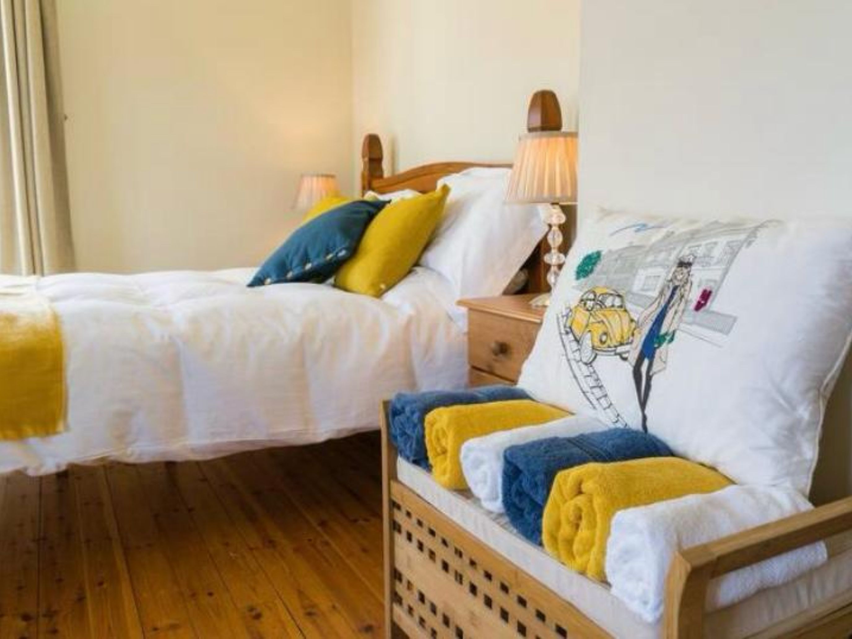 Un lit double avec une tête de lit en bois, une table de chevet avec une lampe et un mur agrémenté d’un coussin décoratif.