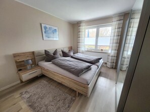 Ein Schlafzimmer mit einem Bett, Nachttischen, einer Lampe, einem Fenster mit Vorhängen und einem Bild an der Wand.