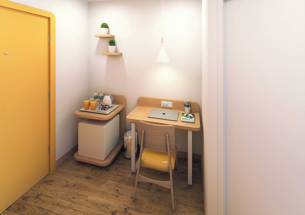 A small room with a yellow door, a wooden desk with a laptop, a chair, and a shelf with plants.