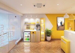 Uma área de recepção moderna com uma máquina de café, um refrigerador e um vaso de planta.