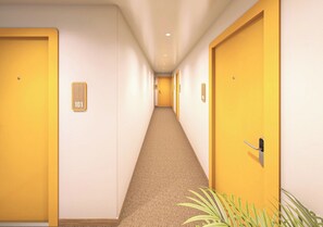 A hotel corridor with doors on both sides, a carpeted floor, and a plant at the end. - Bloom Hotel Fraser Town Bengaluru (Bengaluru)