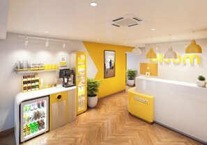 Uma área de recepção com máquina de café, geladeira abastecida com bebidas e balcão com o logotipo 'bloom'.