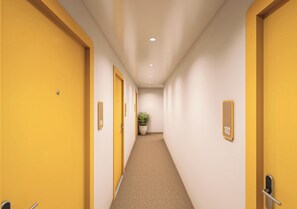 Corredor de hotel com portas amarelas, placas de número de quarto e um vaso de planta.