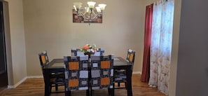 Un comedor con una mesa, sillas, una araña y una cortina con estampado floral.