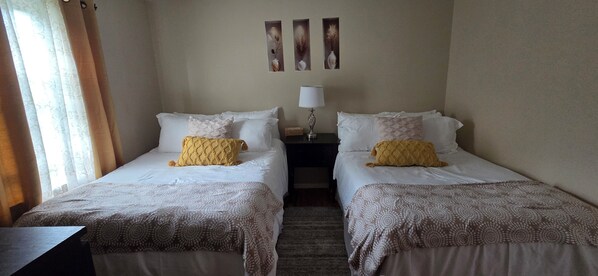 A hotel room with two beds, a nightstand, a lamp, and three wall-mounted paintings.