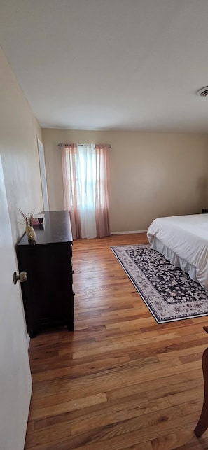 A bedroom with a bed, a dresser, a rug, and a window with curtains.