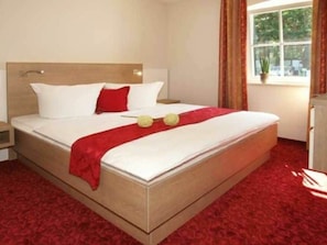 A hotel room with a bed, a nightstand, a window with curtains, and a red carpet. - Holiday Home With 1 Bedroom (Loddin)