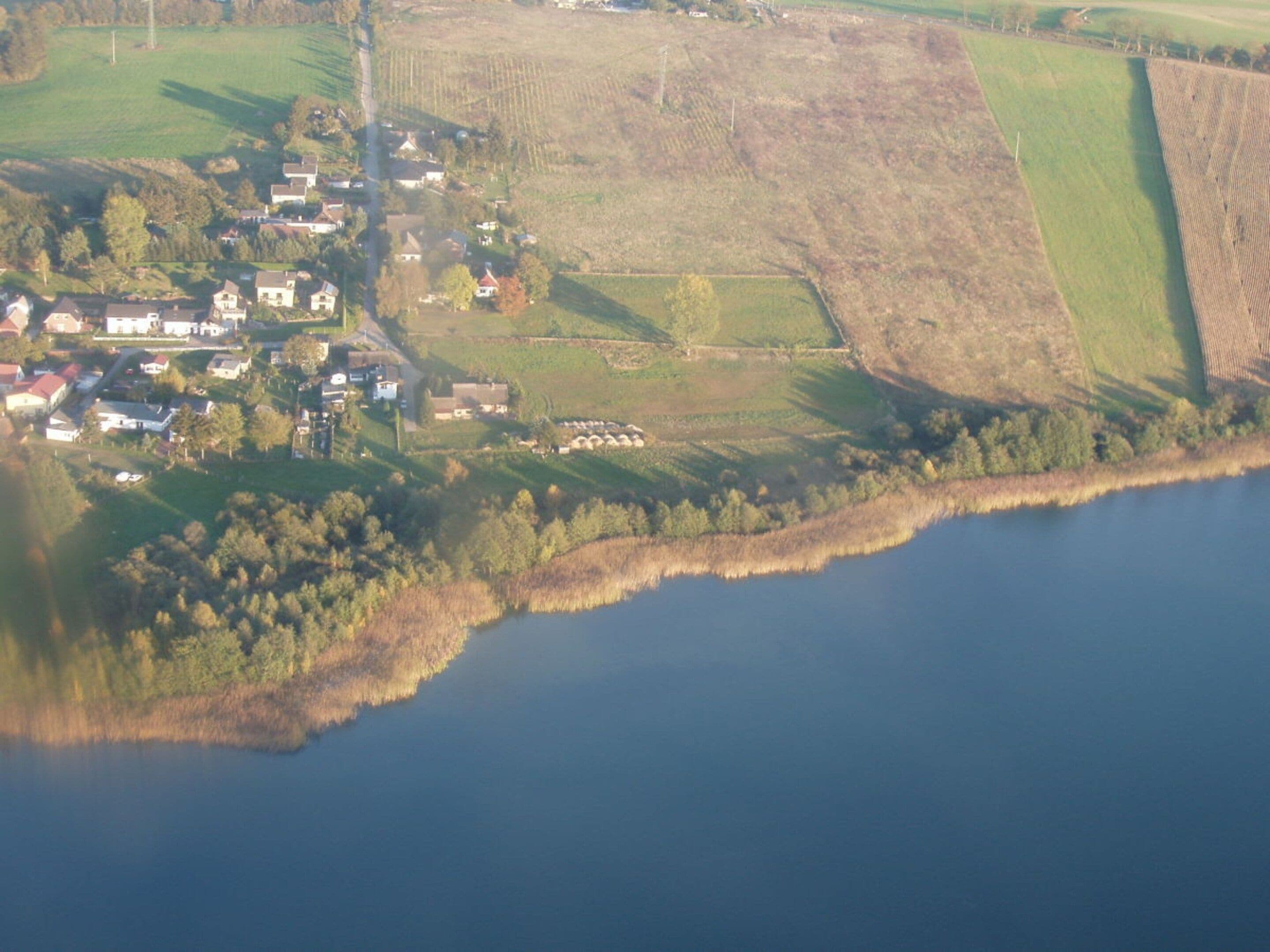 Vista aérea de un pueblo a orillas de un lago, con casas, campos y un muelle.