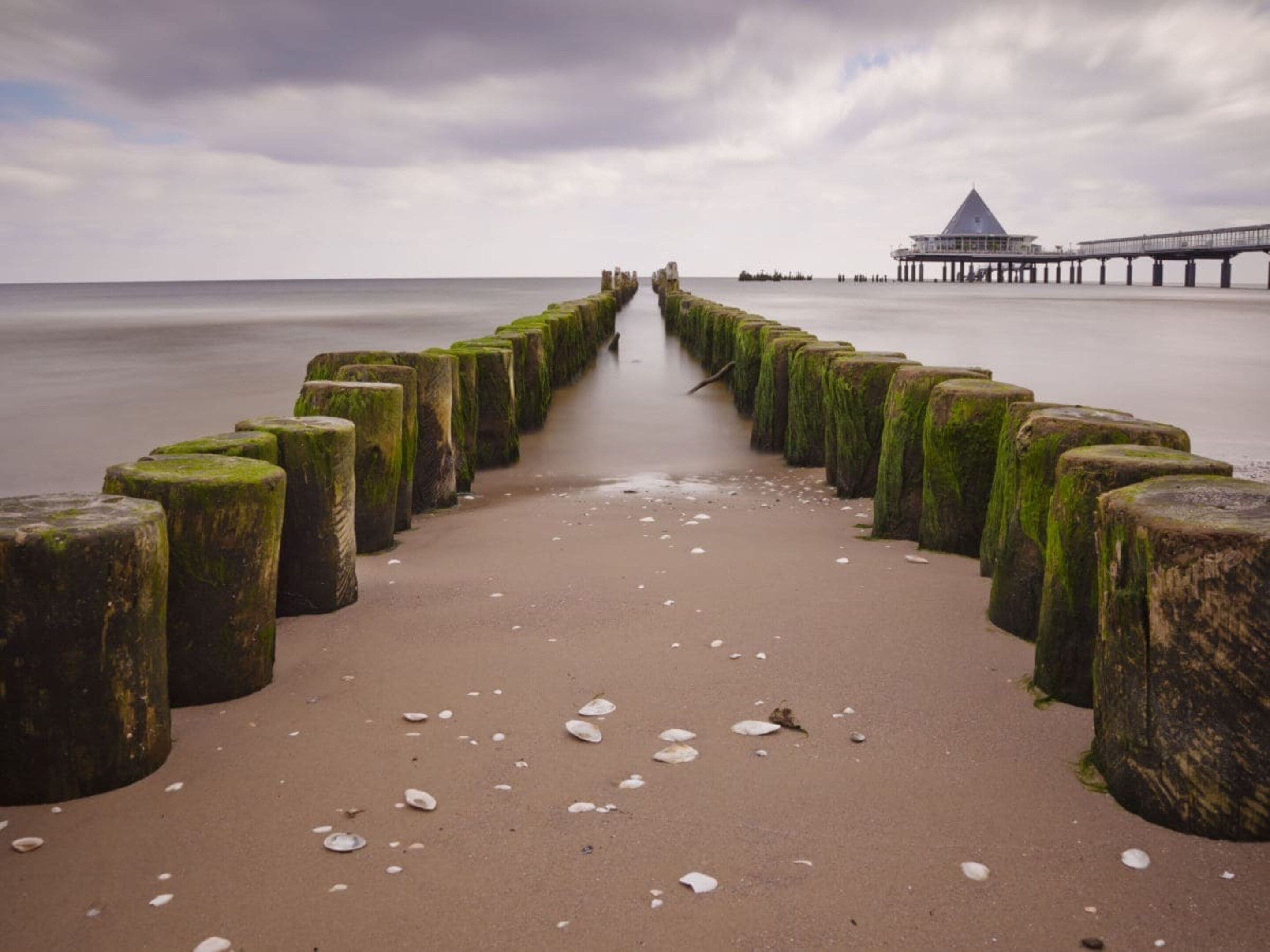 Ein Strand mit einer hölzernen Steg, der zu einem Steg mit einer kegelförmigen Dachkonstruktion führt.