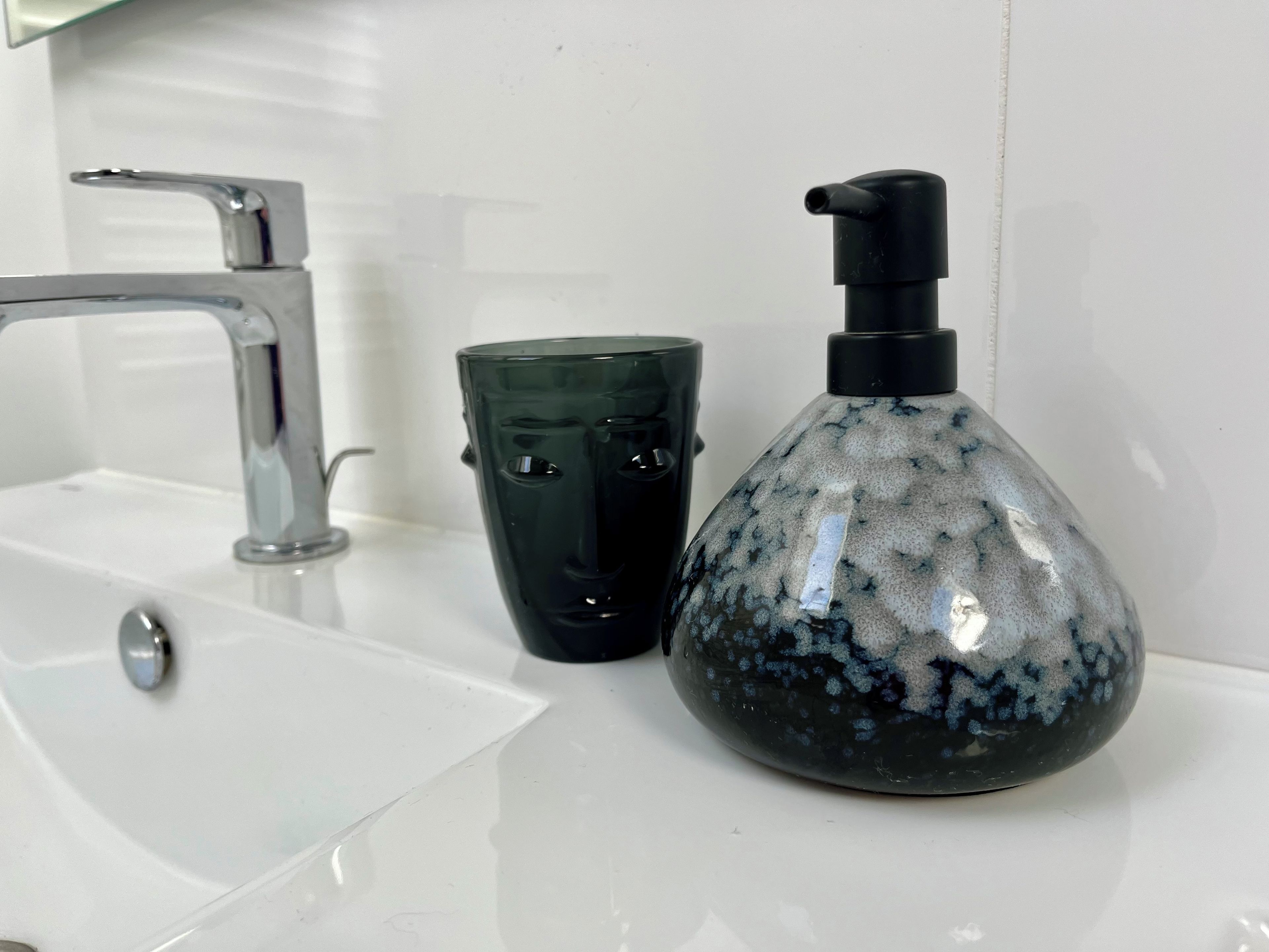 A bathroom sink with a chrome faucet, a green glass cup, and a black soap dispenser.