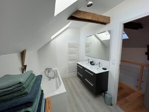 A modern bathroom with a skylight, a large mirror, a white sink, and a wooden ceiling beam. - Bruisse Vacation Rental (Saint-Brieuc-des-Iffs)