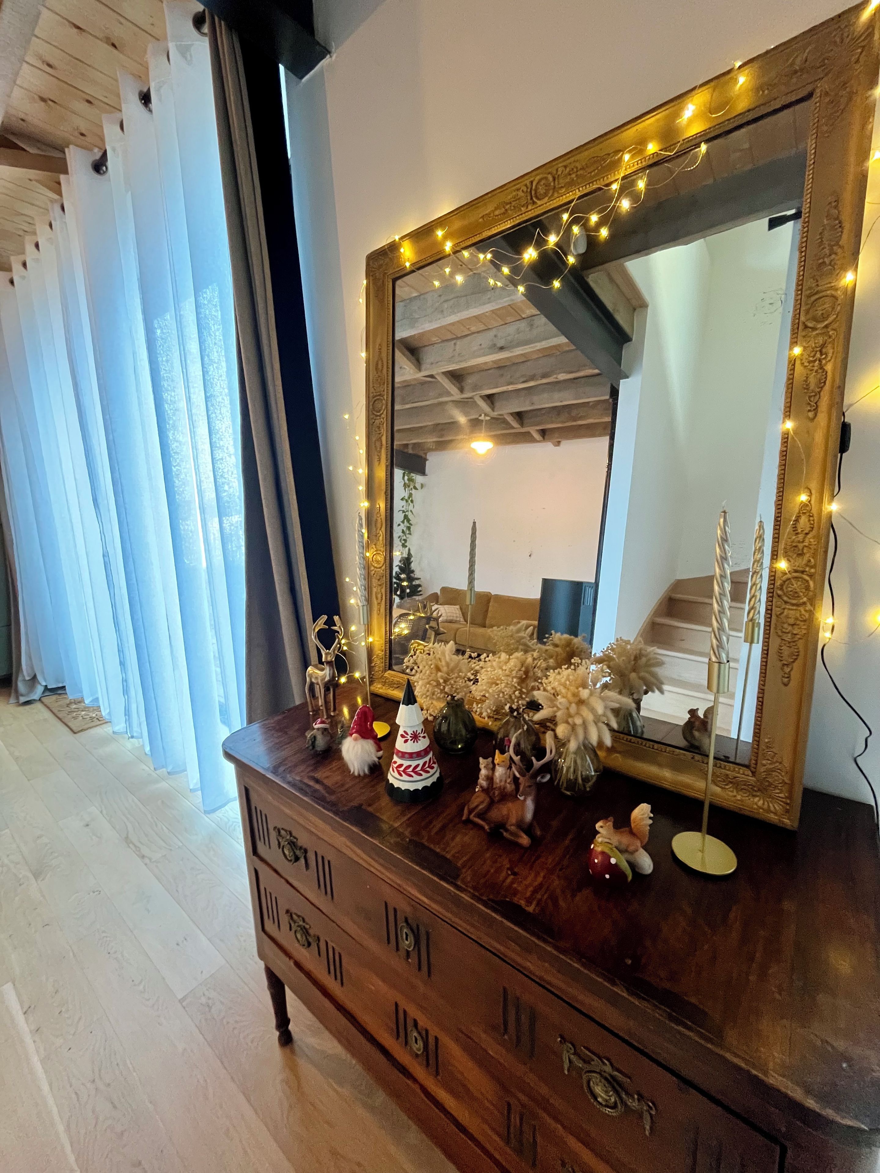 A wooden dresser with a mirror and string lights, decorated with small figurines and flowers.