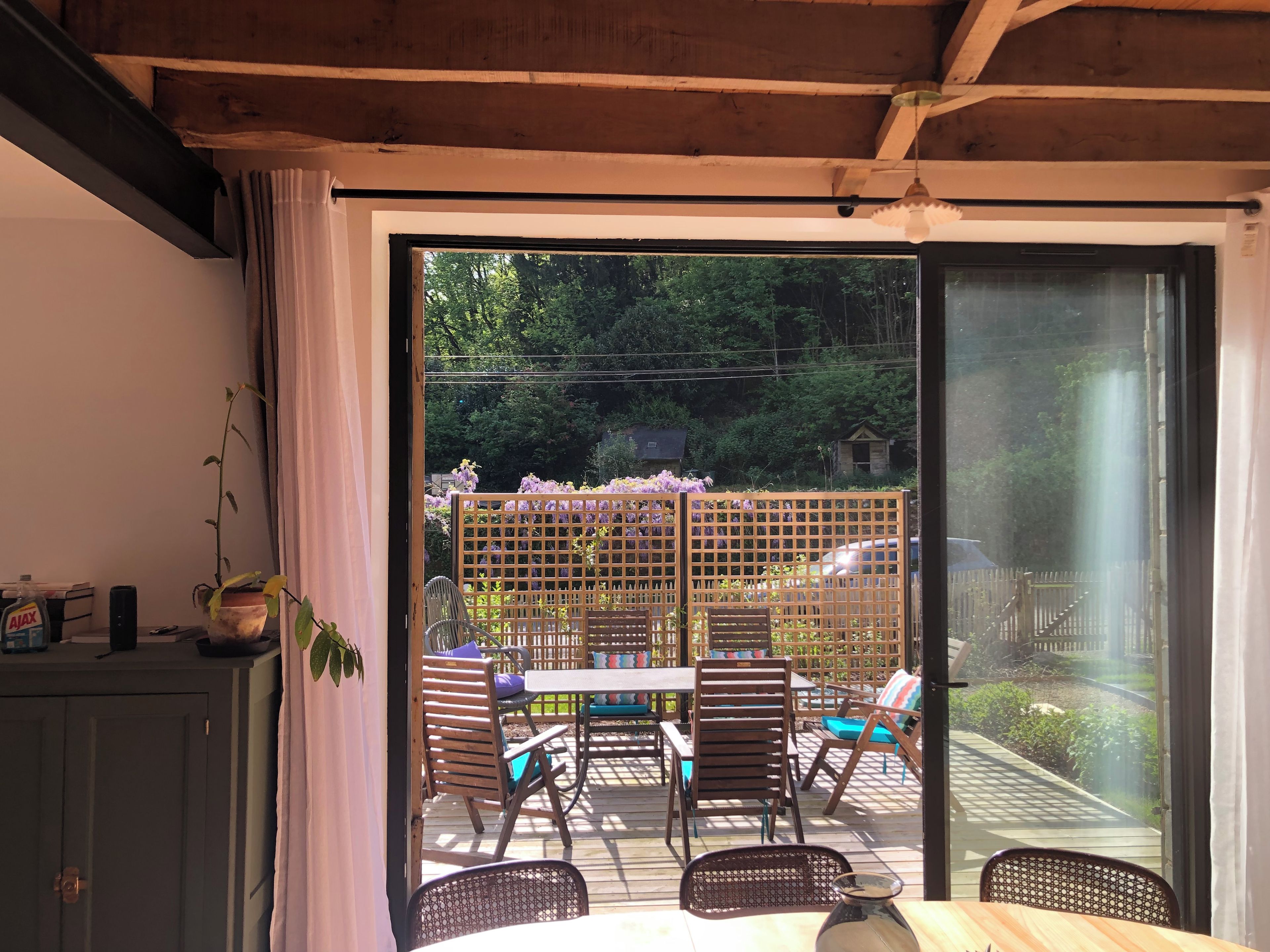 Une pièce dotée d’une porte-fenêtre coulissante donnant sur un patio extérieur aménagé avec une table, des chaises et une clôture en bois.