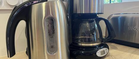 Una tetera eléctrica de acero inoxidable y una cafetera negra sobre una encimera de madera.