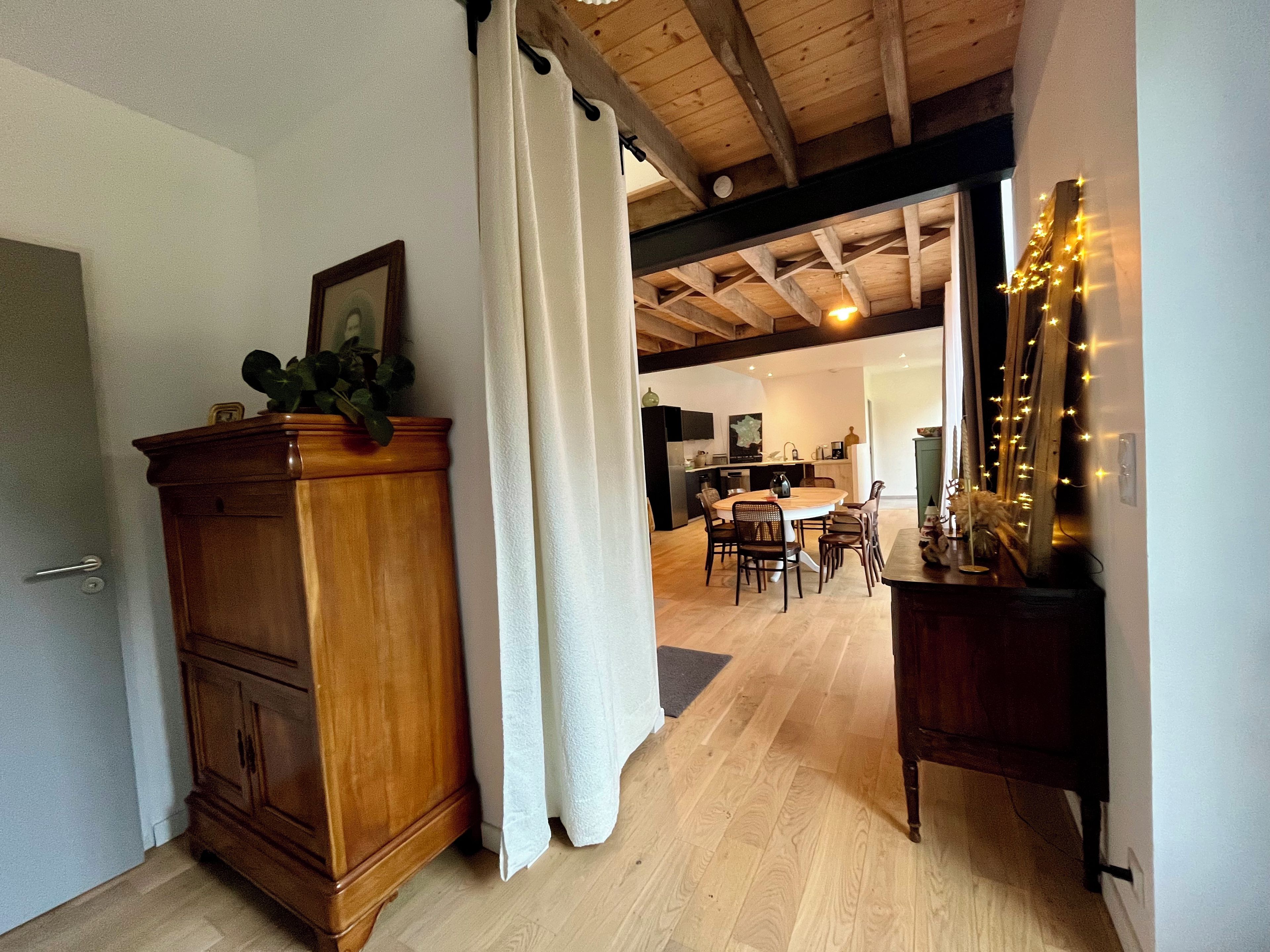 Un meuble en bois avec une plante, un rideau blanc, un coin repas avec une table et des chaises, et un miroir avec des lumières.