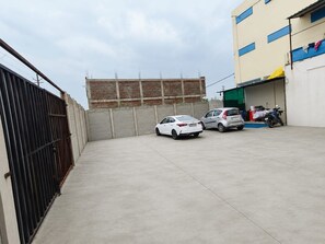 A parking area with a gated entrance, a building with blue windows, and a motorcycle parked inside.