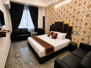 A hotel room with a bed, a sofa, a desk with a lamp, and a wall-mounted air conditioner. - Hotel York Residency (Bhopal)