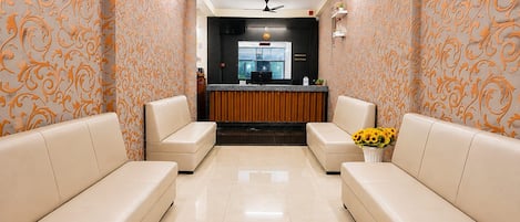 A reception area with a reception desk, two sofas, a ceiling fan, and a vase with sunflowers.