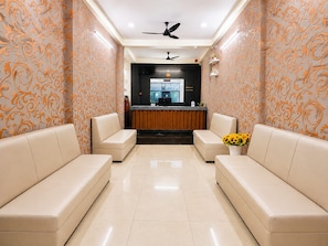 A reception area with a reception desk, two sofas, a ceiling fan, and a vase with sunflowers. - Hotel York Residency (Bhopal)