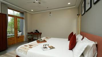 Un dormitorio con cama, escritorio y silla. Hay una ventana con cortinas, un ventilador de techo y una obra de arte enmarcada en la pared.