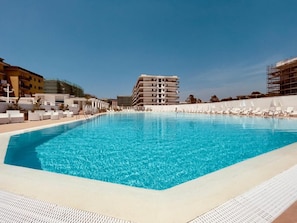 Una piscina con sillas de descanso y un edificio al fondo.
