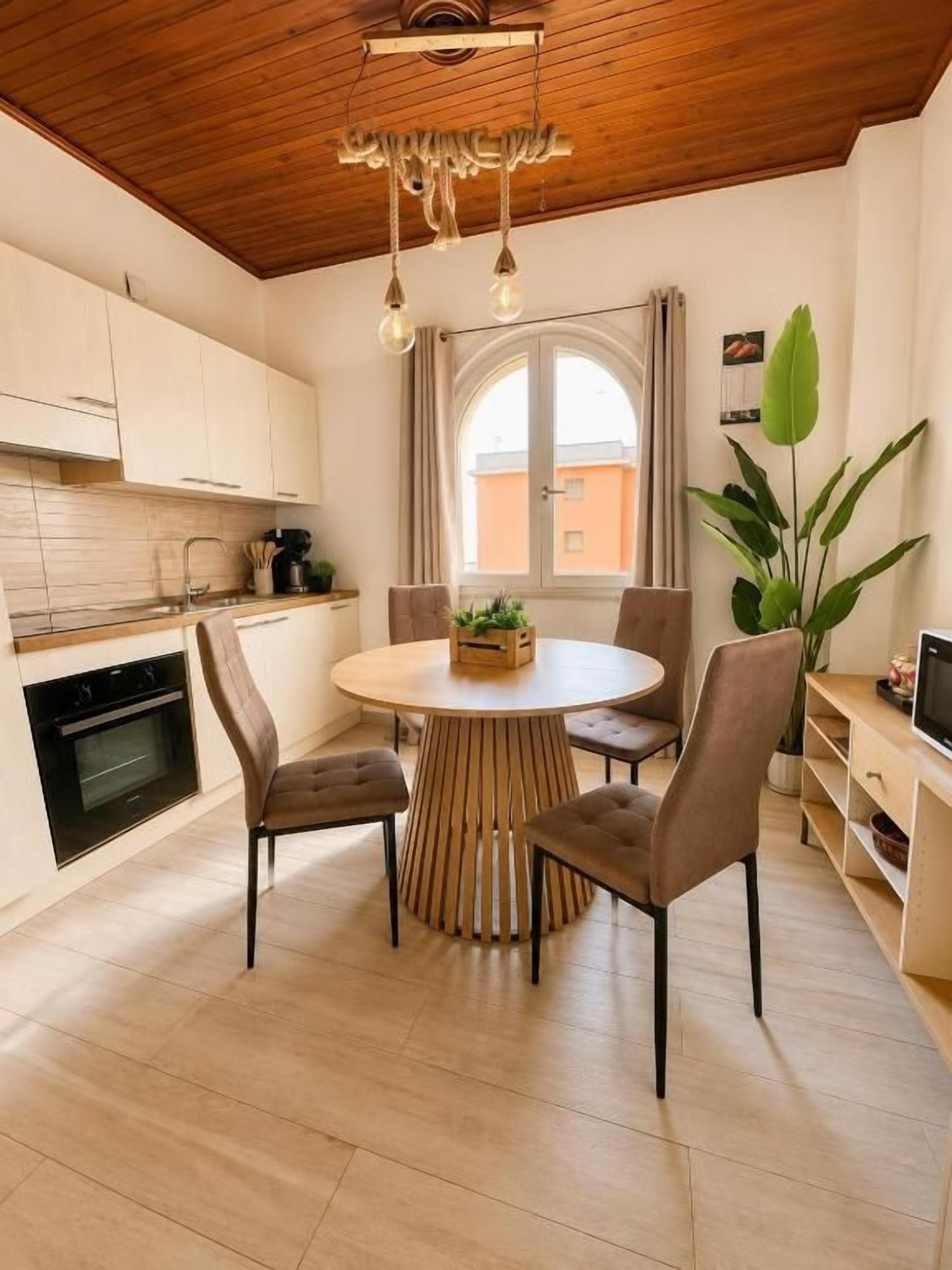 Una cocina moderna con armarios de madera, una mesa redonda con sillas y un amplio ventanal con cortinas.