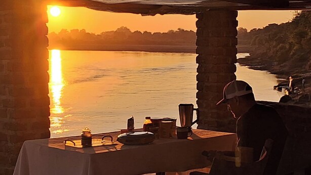 A table set up outdoors with a view of a body of water during sunset. - Mikango New Dream Safari (South Luangwa National Park)