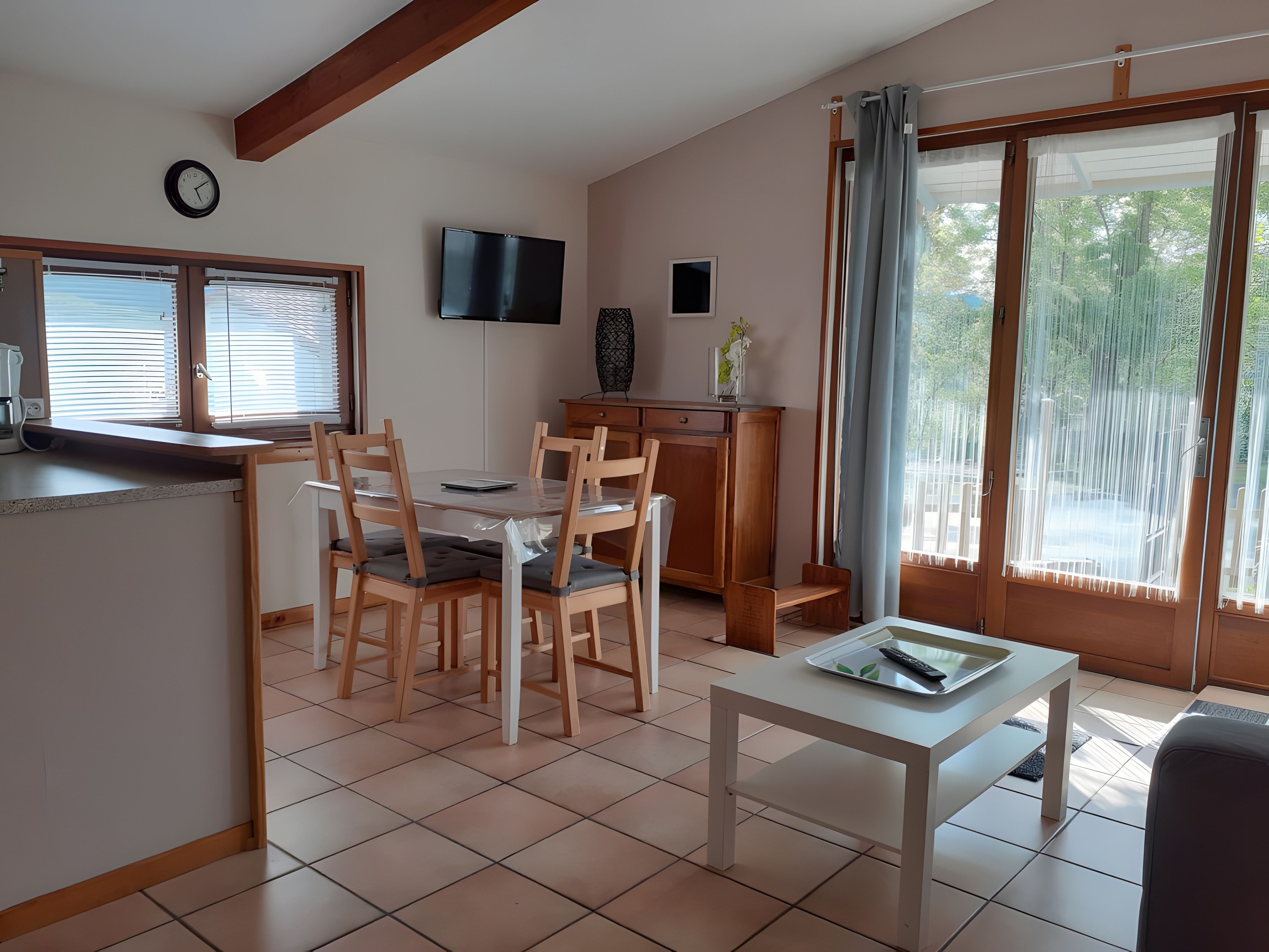 A dining area with a table and chairs, a television on the wall, and a window with curtains.