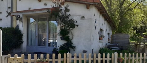 Un edificio blanco con techo de tejas, cerca de madera y plantas en macetas.