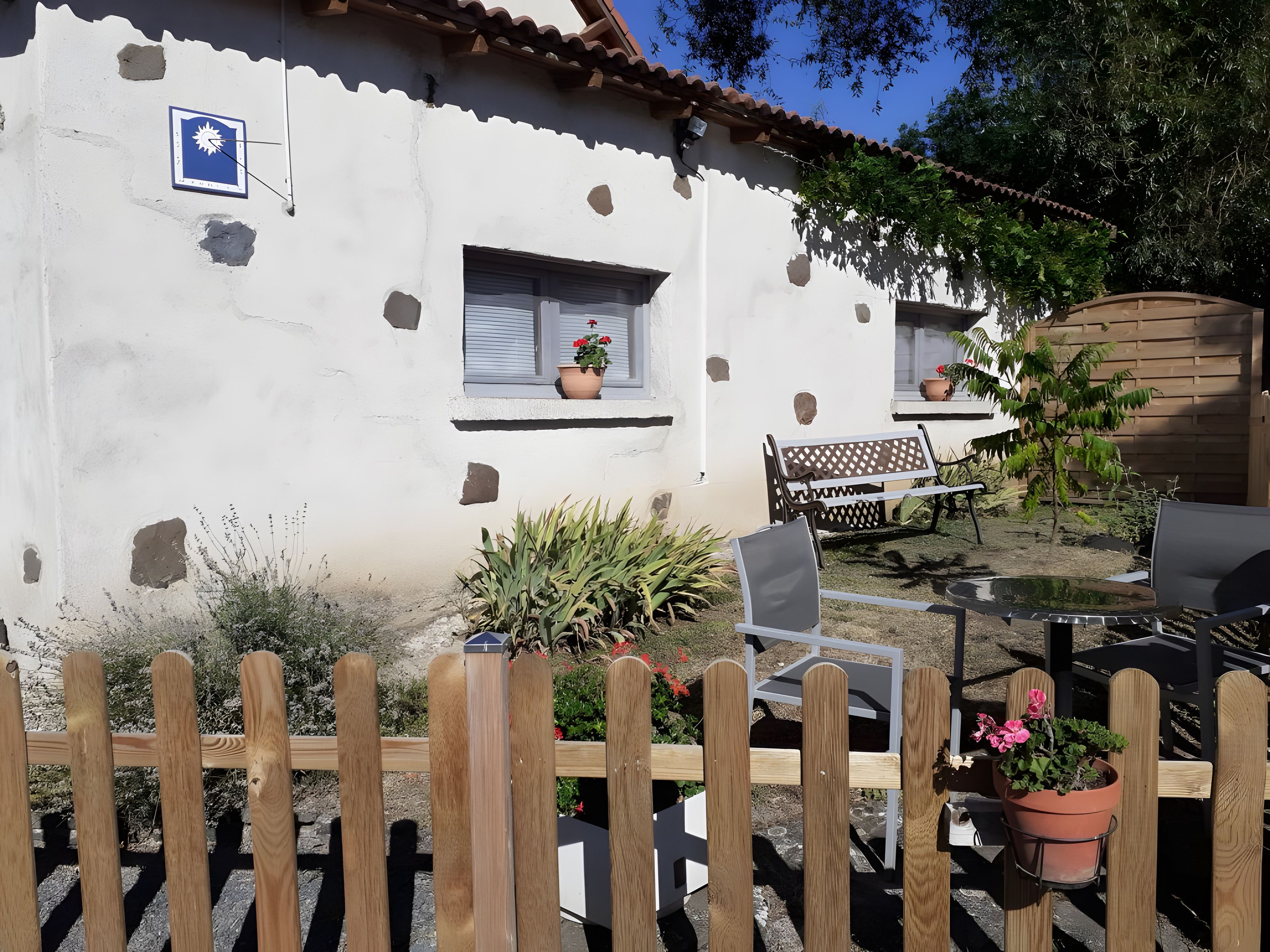 A white building with a blue sign, a wooden fence, and outdoor furniture.