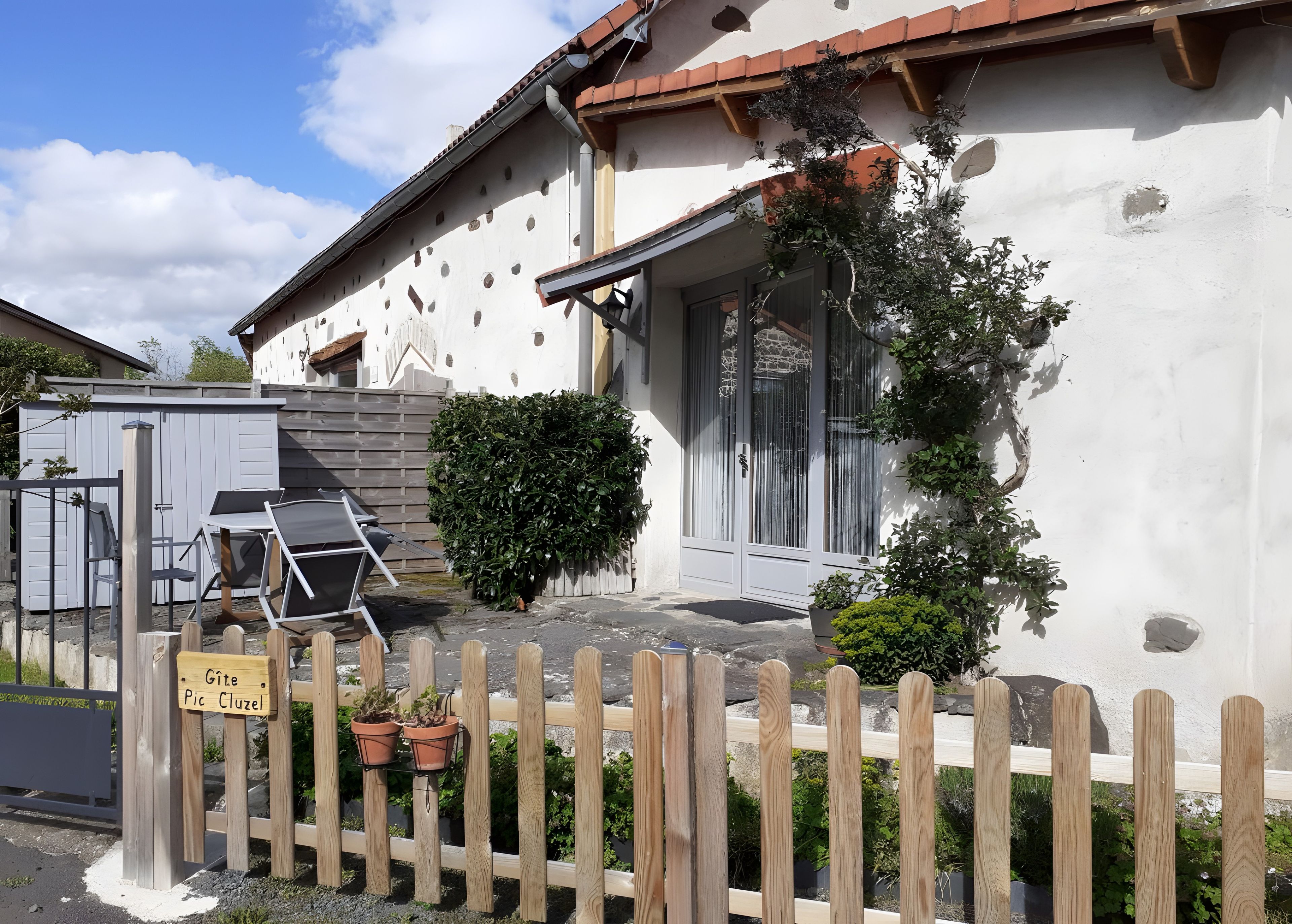A house with a white exterior, a wooden fence, and a sign that reads 'Gite Pic Cluzel.'