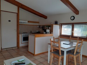 A kitchen with a dining area, wooden beams, a clock, and a window with blinds.