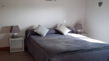 A bedroom with a bed, two bedside tables, a lamp on each table, a wall hanging, and a heart-shaped decoration.