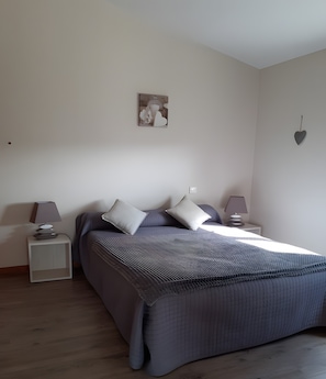 A bedroom with a bed, two bedside tables, a lamp on each table, a wall hanging, and a heart-shaped decoration.