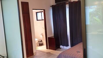Una habitación con una cama, una silla, una mesa, un ventilador de techo y un ventanal.